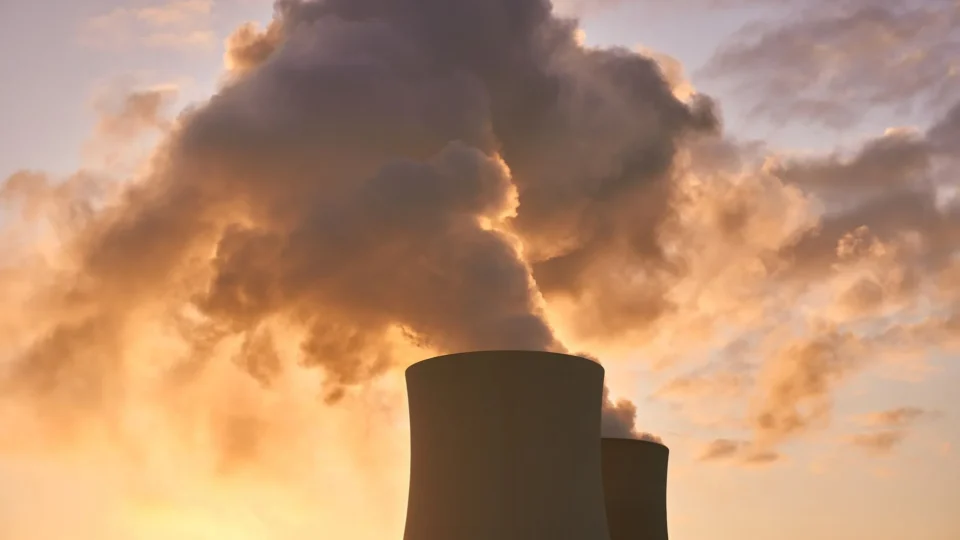 Cooling towers release smoke into a dramatic sunset sky, highlighting environmental impact.