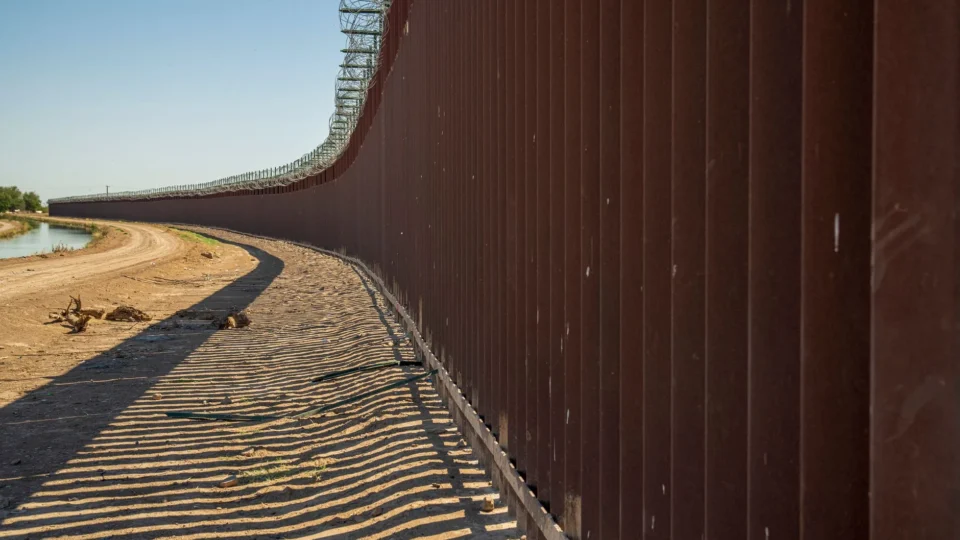 Long view of a steel border wall under clear skies, emphasizing solitude and division.