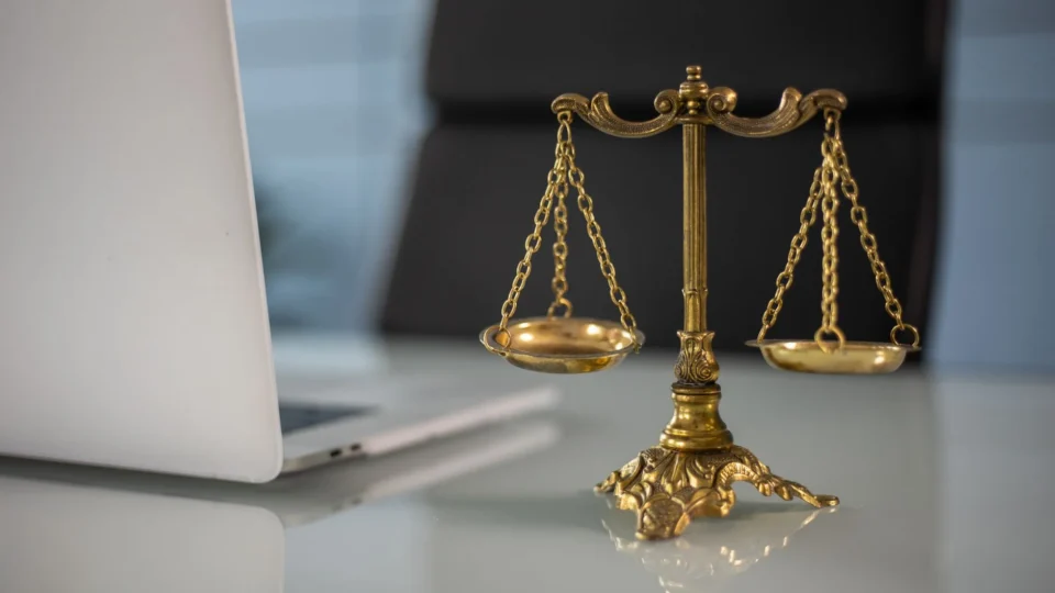 Golden justice scales on a desk beside a laptop, symbolizing law and balance.