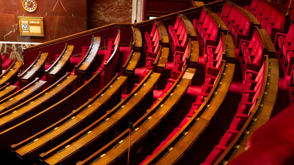 A luxurious interior view of a legislative chamber with curved red seating and wooden desks.