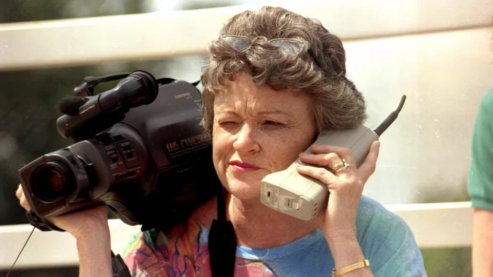 A journalist holding a video camera and a phone
