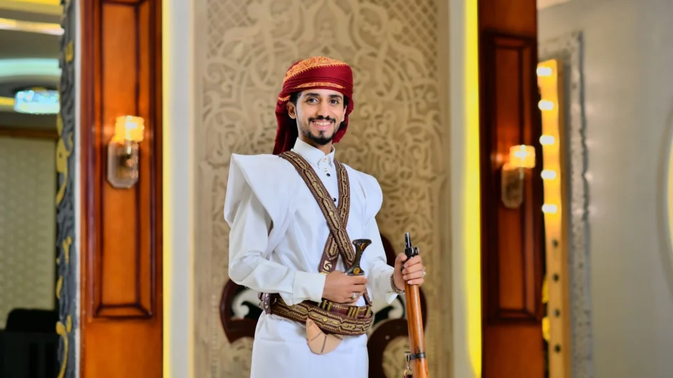 Man in traditional Saudi Arabian attire with ornate decor in Makkah Province setting.