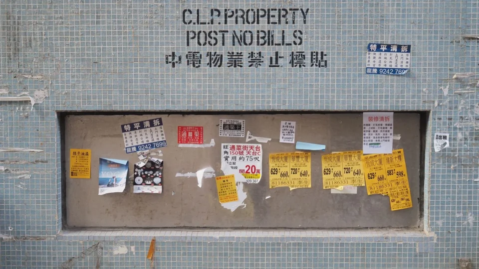 City wall with various multilingual posters in Hong Kong, depicting urban life and culture.