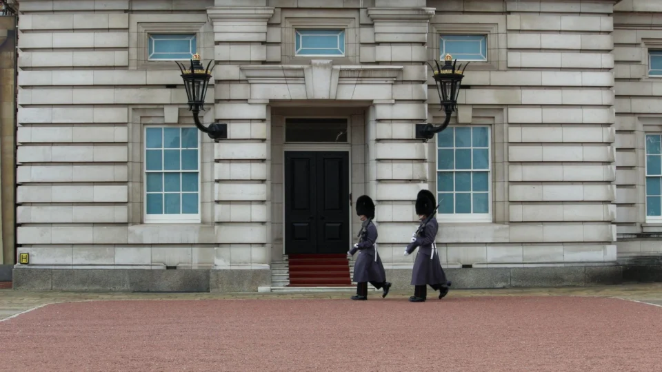 Two royal guards in traditional attire march at Buckingham Palace, London.