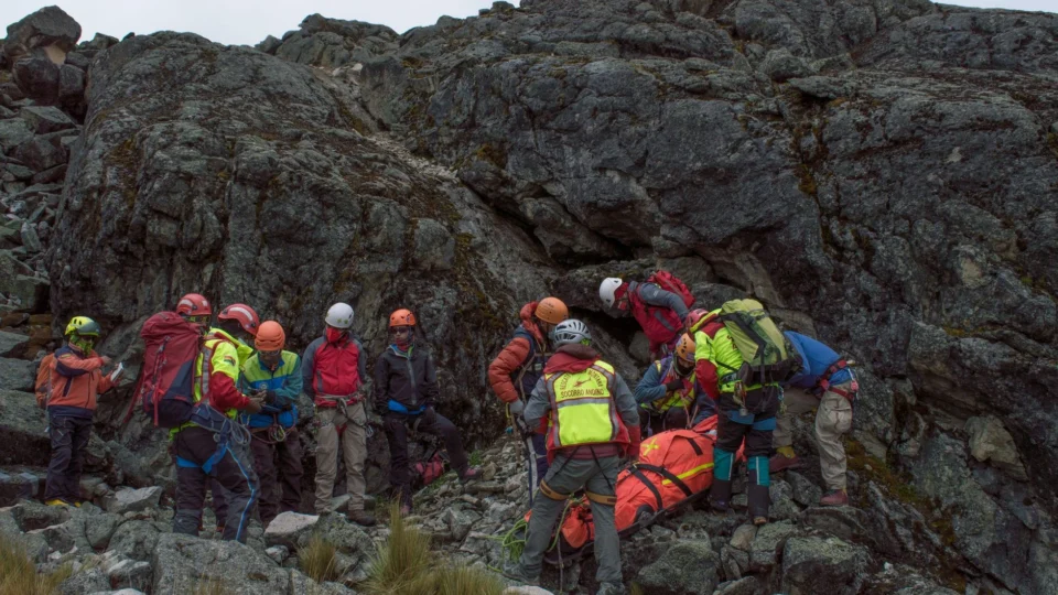 A rescue team aids an injured hiker on a rocky mountain slope during daylight.