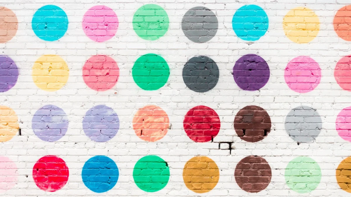 Vibrant polka dot pattern mural on a textured white brick wall.