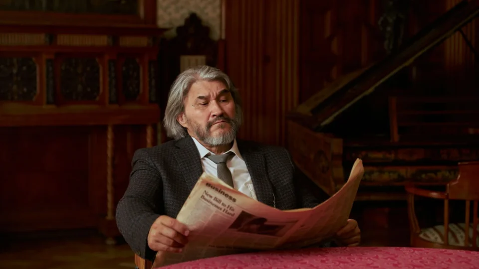 Senior man in a suit reading a newspaper in a luxurious, vintage styled room.