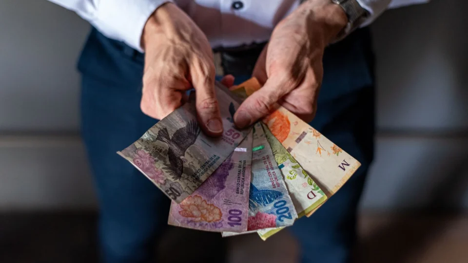 Closeup of a person holding various Argentine peso banknotes, highlighting financial concepts.