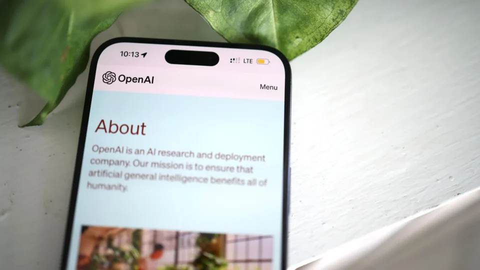 Close-up shot of a smartphone screen showing the OpenAI website with greenery in the background.