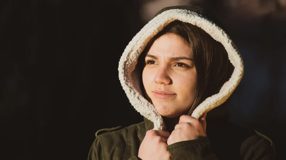 Portrait of a young woman in a hooded coat, looking thoughtful outdoors.