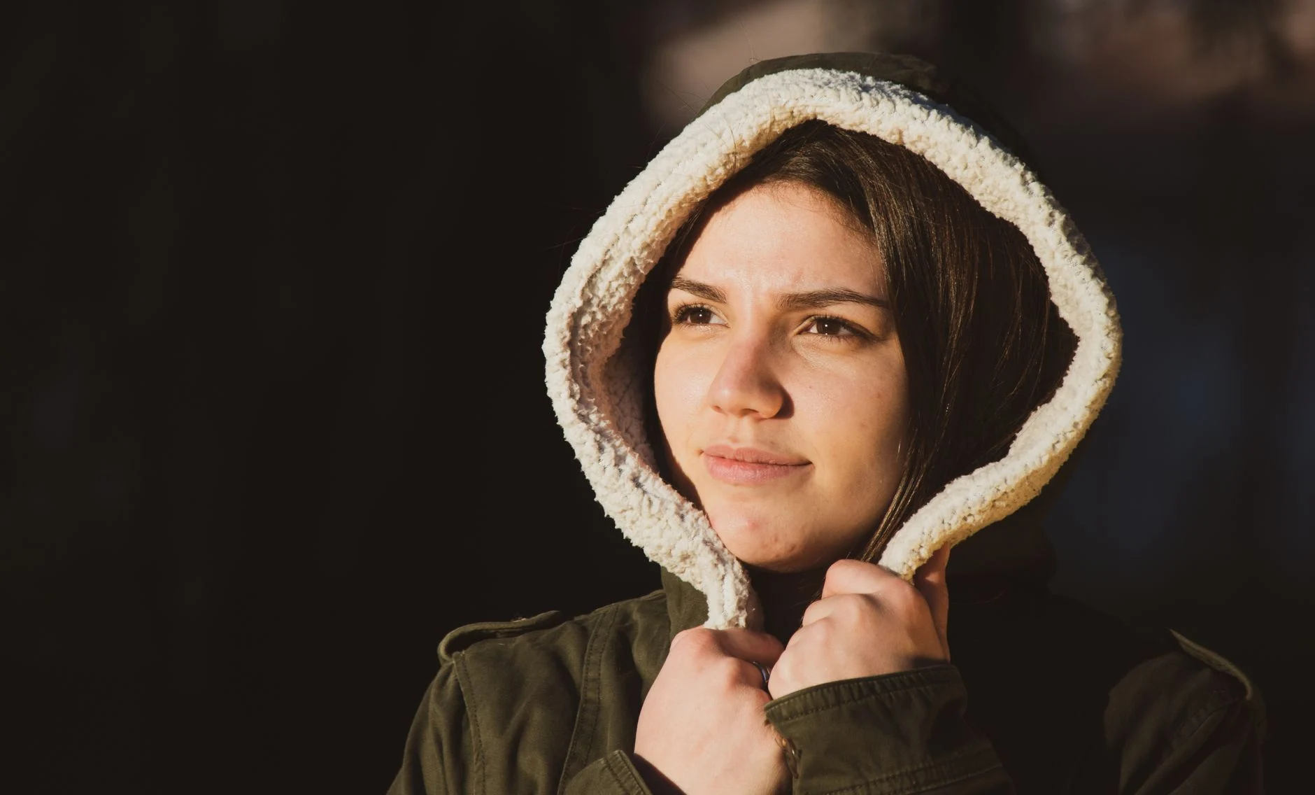 Portrait of a young woman in a hooded coat, looking thoughtful outdoors.