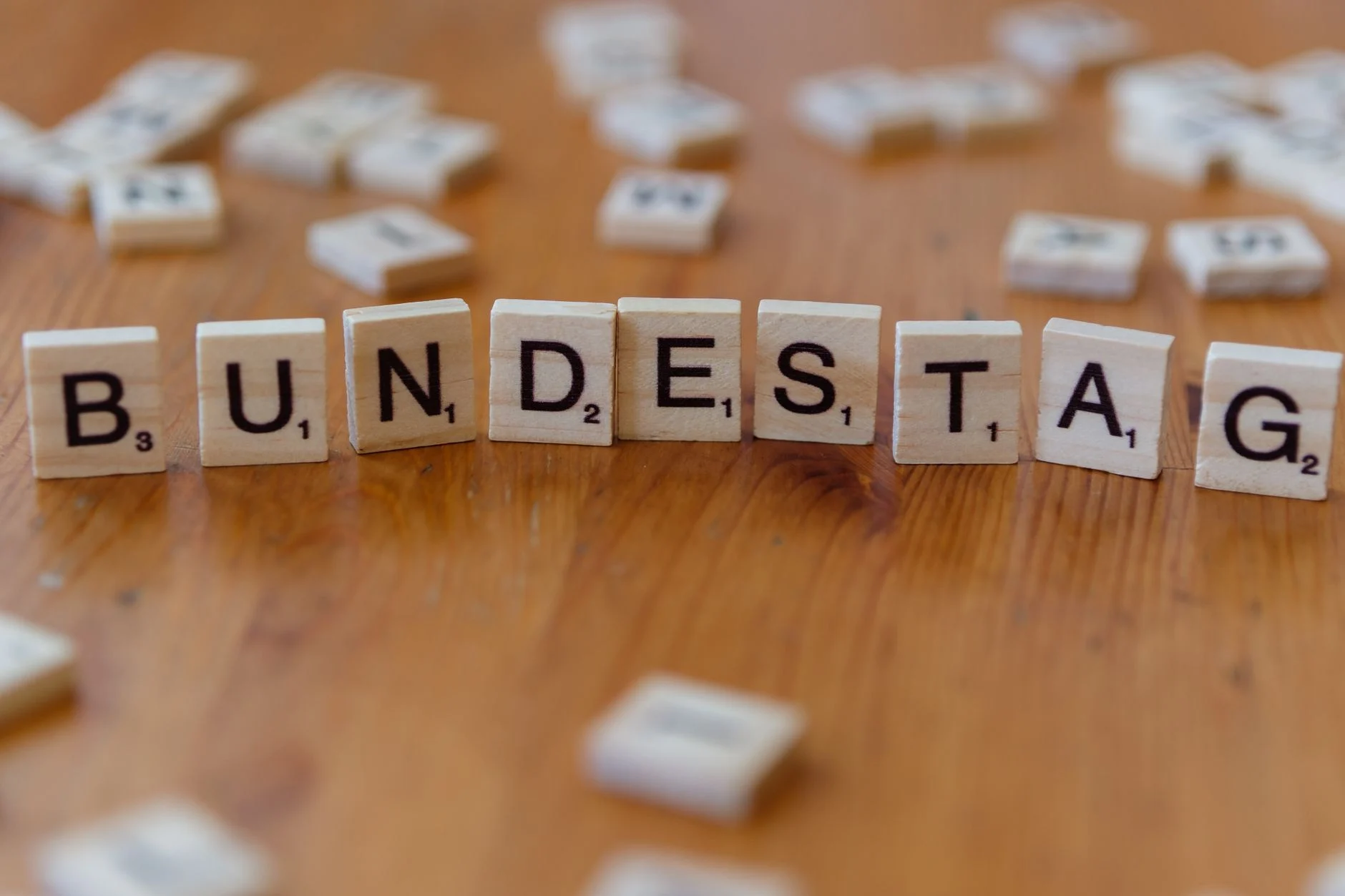 Wooden Scrabble tiles spelling 'Bundestag' on a rustic table, symbolizing German politics.