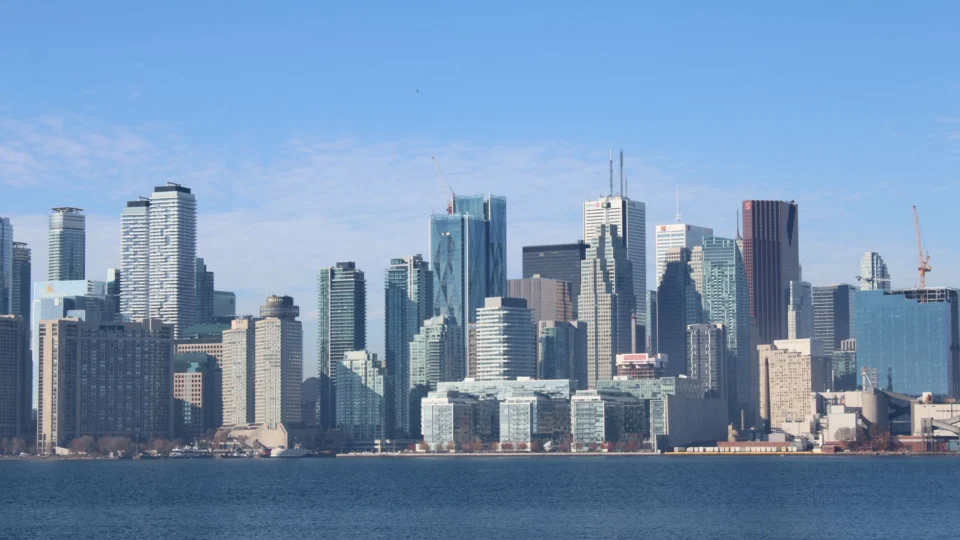 Beautiful cityscape of Toronto with modern skyscrapers reflecting in the water under a clear blue sky.
