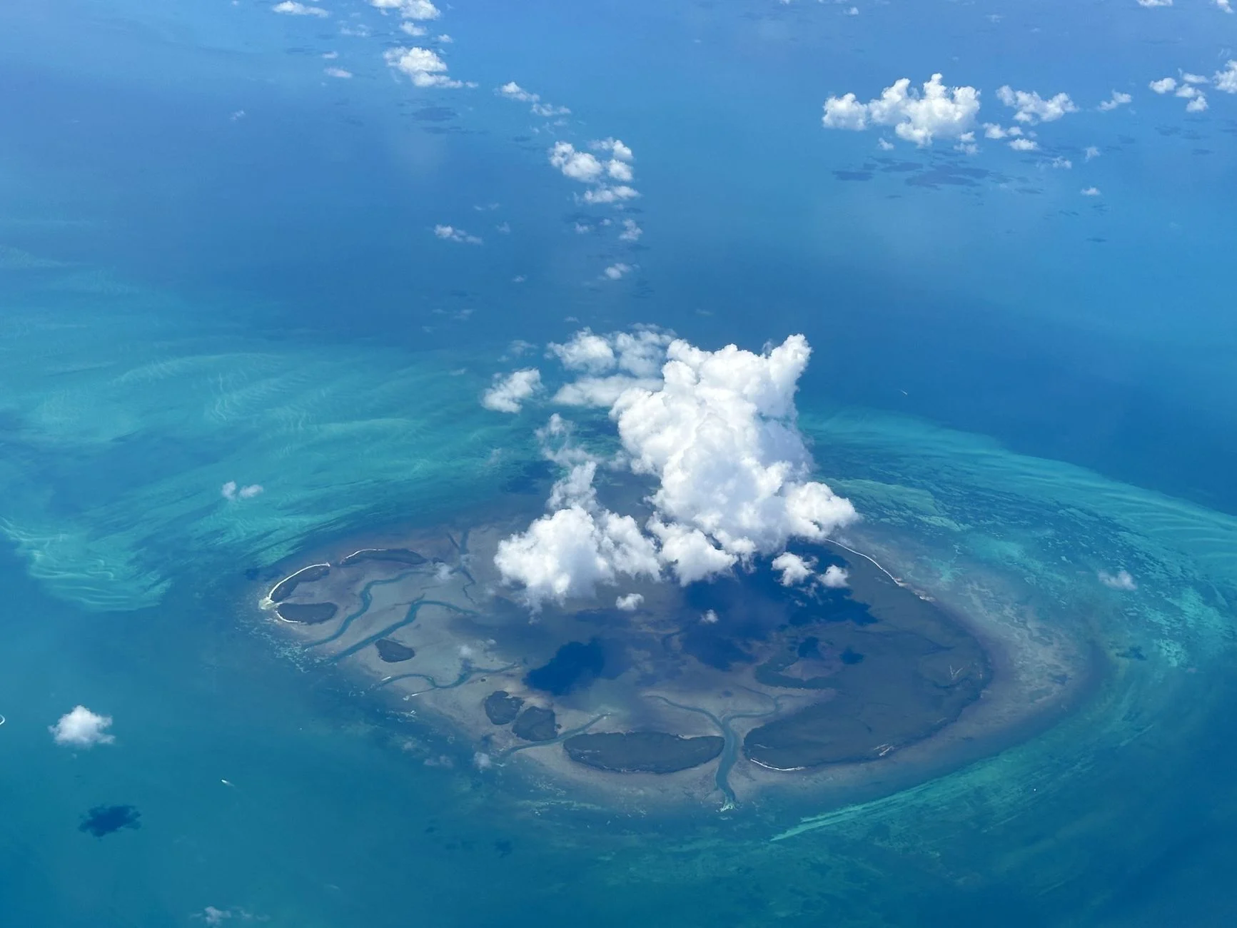 Stunning aerial view of a secluded tropical island surrounded by turquoise waters and clouds.