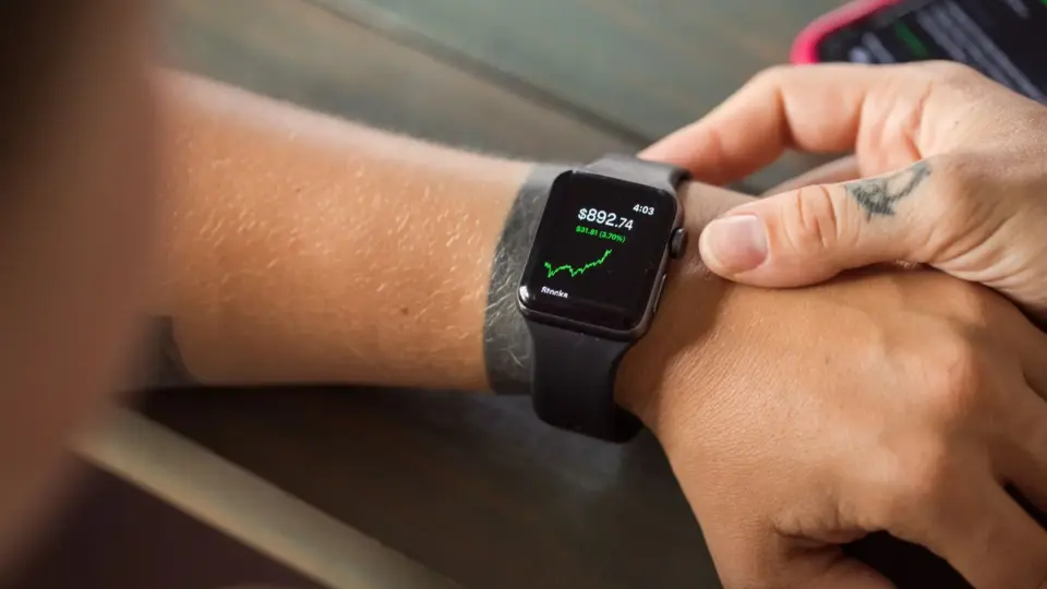Close-up of a smartwatch showing stock market data, with hands wearing it.