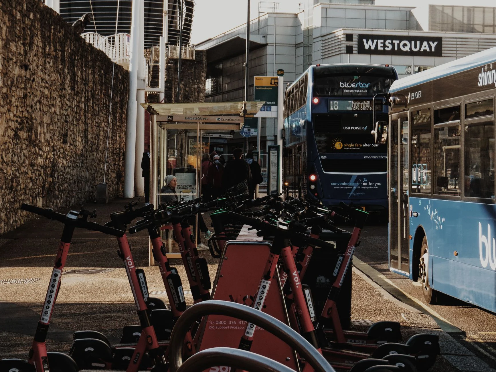 Bustling bus stop with electric scooters and buses near Westquay, England.