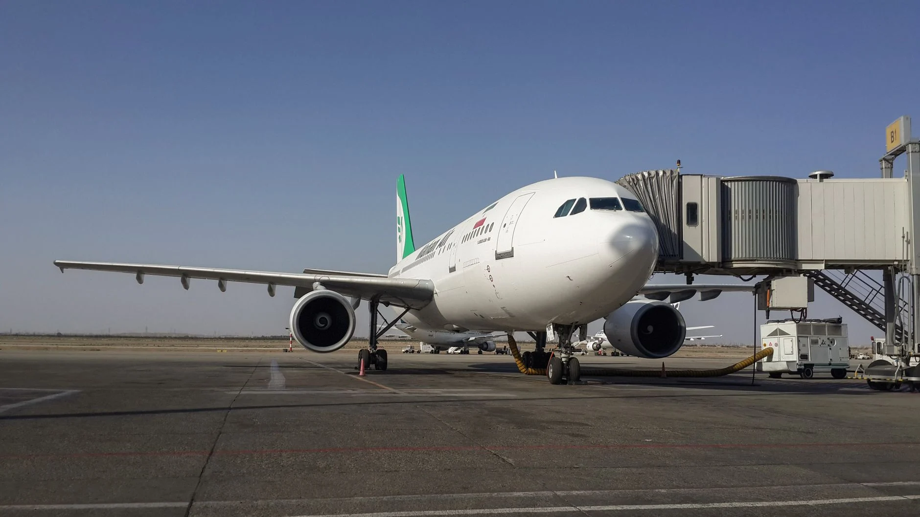 A parked airplane at Tehran Imam Khomeini Airport connected to a jetway on a clear day.