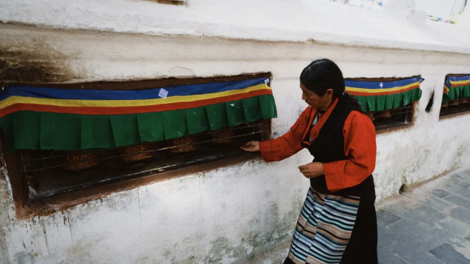 A woman in traditional attire spins prayer wheels in Kathmandu, Nepal, at a Buddhist site.
