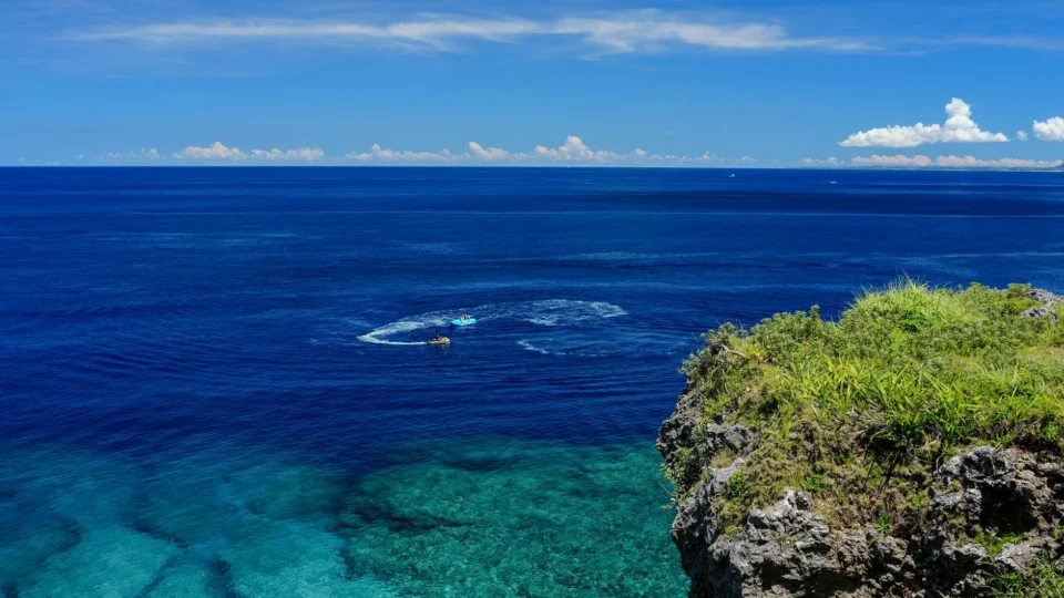 Breathtaking view from an Okinawa cliff overlooking the serene, crystal-clear sea under a vibrant blue sky.