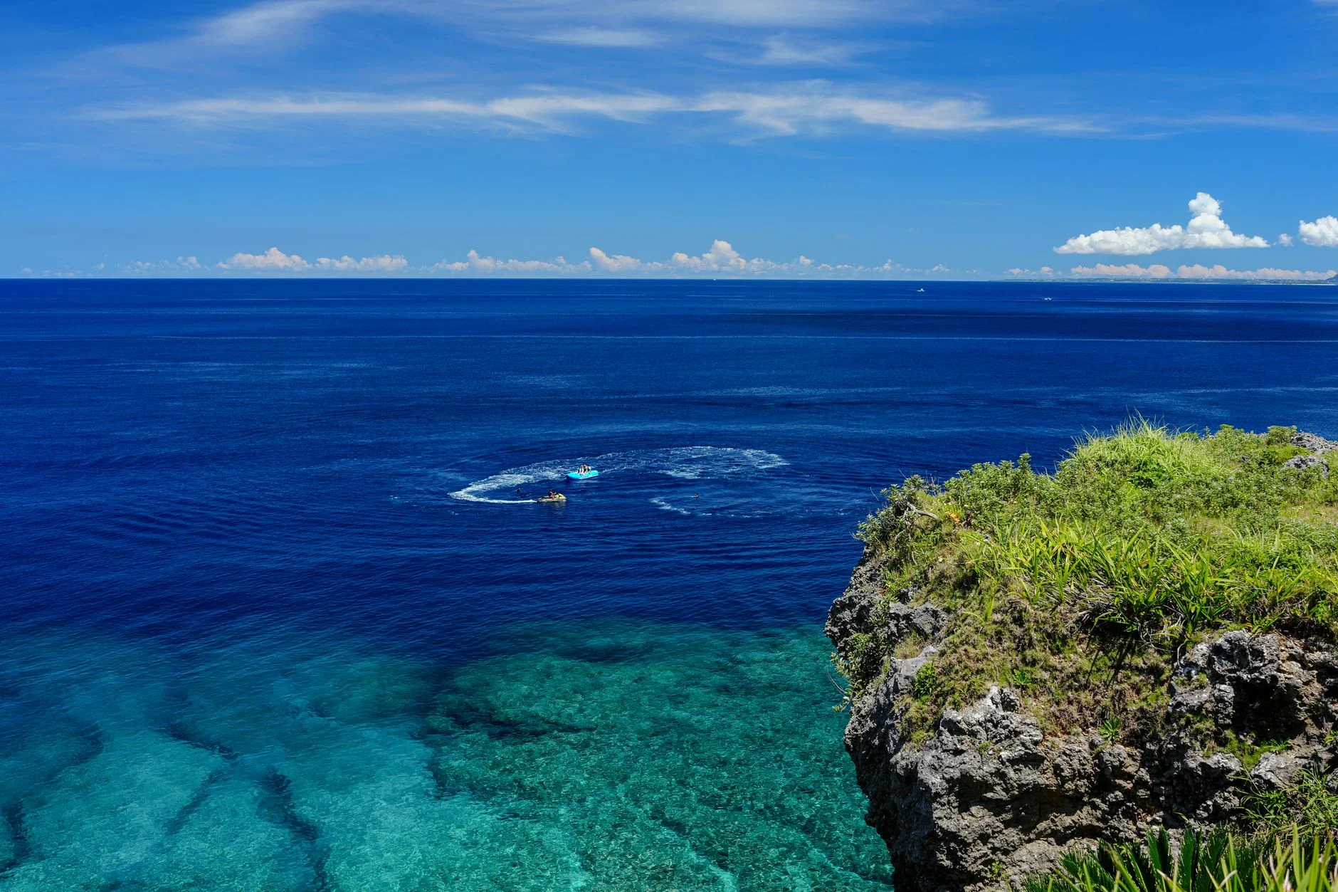 Breathtaking view from an Okinawa cliff overlooking the serene, crystal-clear sea under a vibrant blue sky.