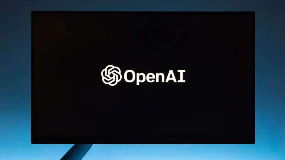 Minimalist display of OpenAI logo on a screen, set against a gradient blue background.