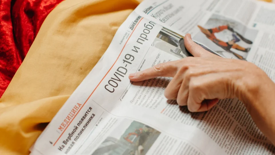 A close-up shot of a hand pointing at a COVID-19 headline in a newspaper.