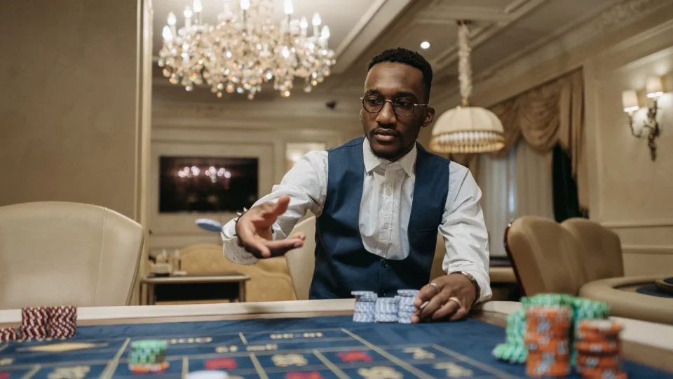 A man in formal attire plays roulette in a luxurious casino under a chandelier.