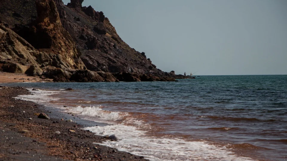 Waves crash on the rocky shore of Hormoz Island, Iran with clear blue skies.