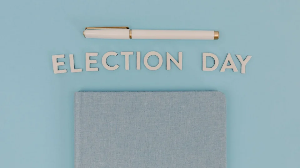 Blue notebook and pen against a light blue background reading 'Election Day', ideal for campaign themes.