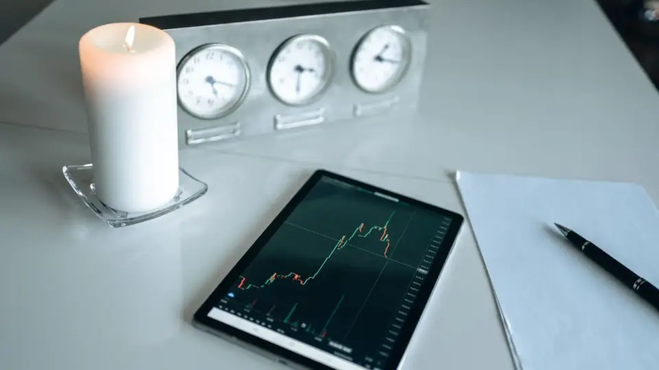 Minimalist desk setup with tablet showing trading graph alongside candle and clocks.