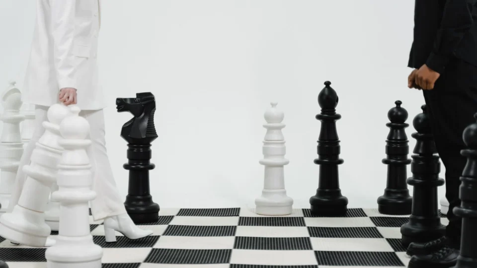 Two individuals strategize over a life-sized chess game indoors.