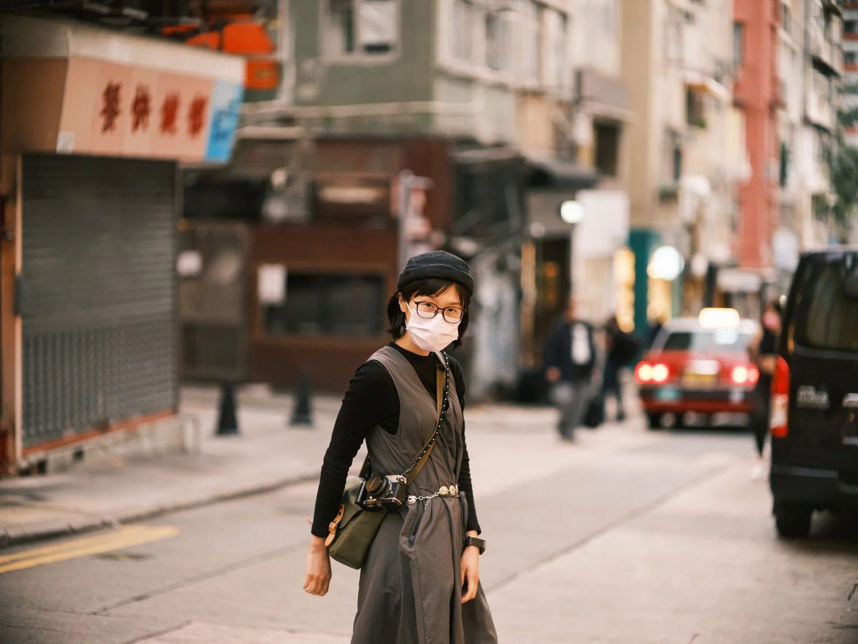 A woman wearing a mask and glasses walks along a bustling street on Hong Kong Island.