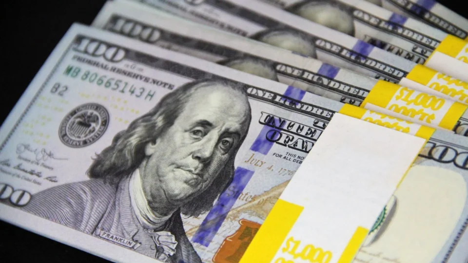 Close-up of stacked US hundred dollar bills on black surface, emphasizing wealth and finance.