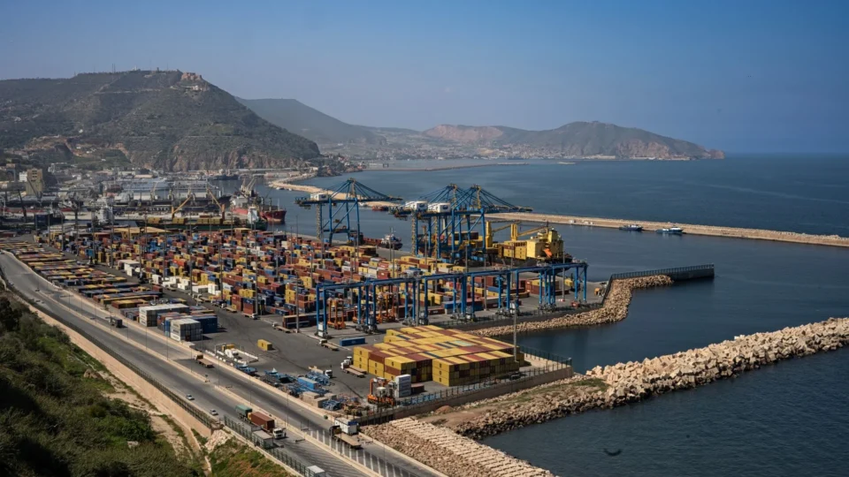 Port of Oran showing containers, cranes, and Algerian coastline in the background.