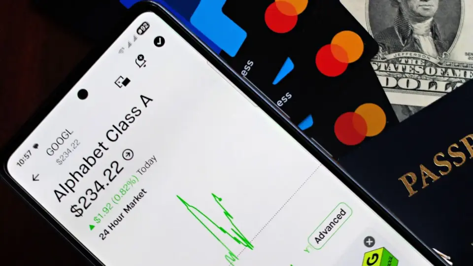 A smartphone displaying Alphabet stock price alongside credit cards, cash, and passport.