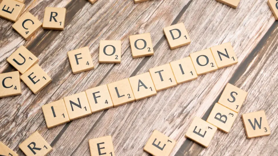 Wooden scrabble tiles arrange to spell 'Food Inflation' on a rustic wooden surface, conceptually depicting rising food prices.