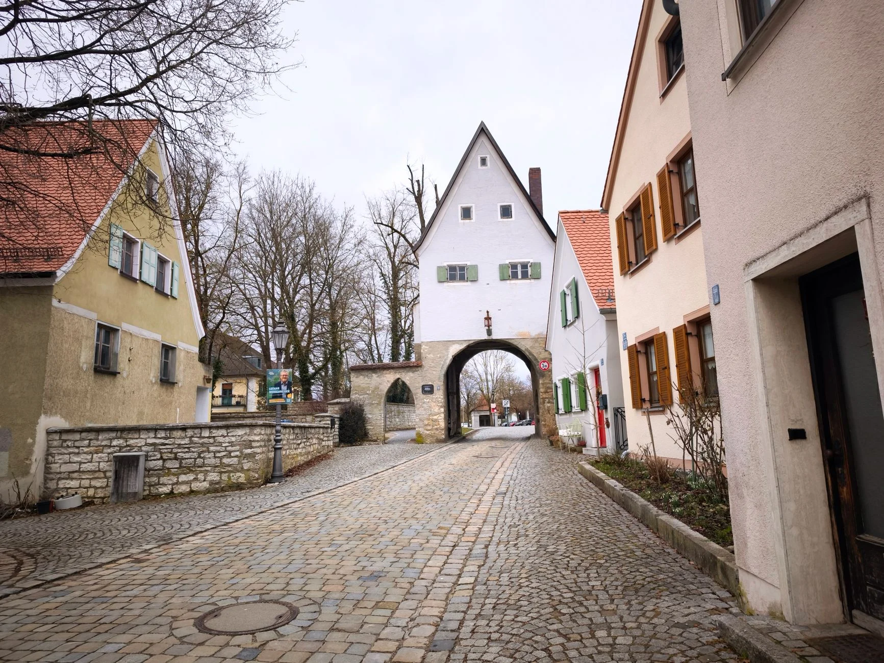 Picturesque view of a cobblestone street with historic houses and archway in a quaint European town.