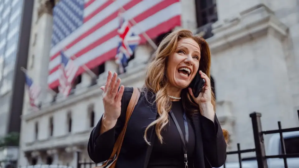 Businesswoman talking on a smartphone, laughing, with American flag background.