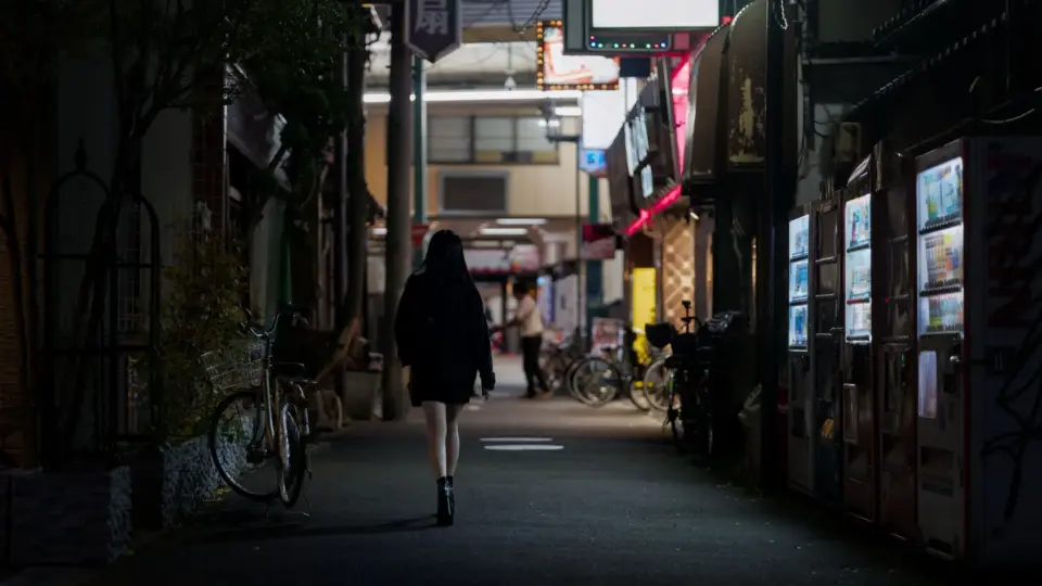 A woman walks down a dimly lit street in Osaka, Japan, lined with vending machines.
