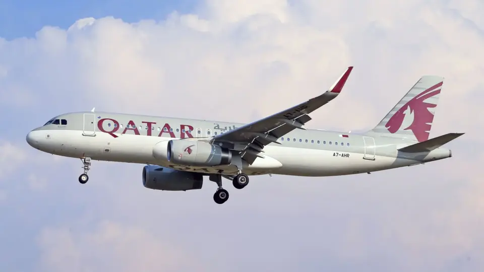 Qatar Airways Airbus A320 aircraft against a clouded sky, captured mid-flight.